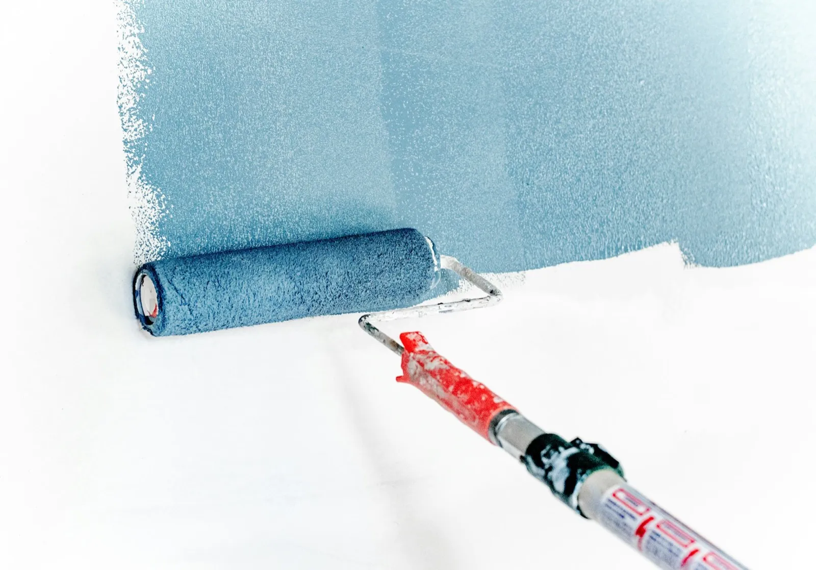 A roller laying a coat of blue paint onto a white wall.